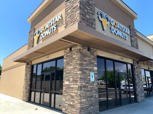 Exterior of Goatstar Donuts shop with a stone facade and large windows on a sunny day.