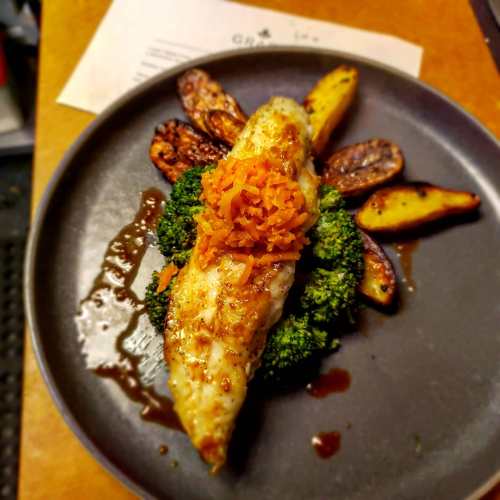 A plate featuring a fillet of fish on a bed of broccoli, garnished with carrots, alongside roasted potato wedges.