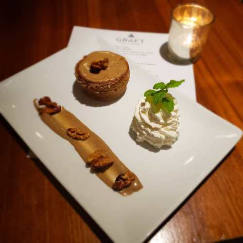 A dessert plate featuring a caramel cheesecake, whipped cream, and a caramel sauce with nuts, set on a wooden table.