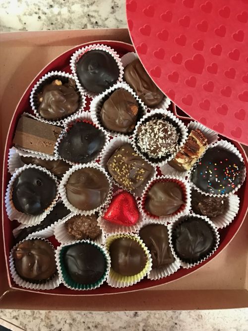 A heart-shaped box filled with assorted chocolates, including truffles, bars, and decorated treats.