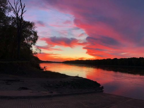 A serene river at sunset, with vibrant pink and purple clouds reflecting on the water's surface.