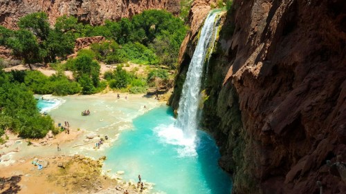A stunning waterfall cascades into a turquoise pool surrounded by lush greenery and people enjoying the natural beauty.