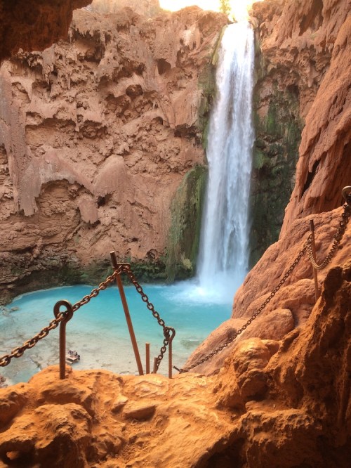 A stunning waterfall cascades into a turquoise pool, surrounded by rocky cliffs and chains for safety.