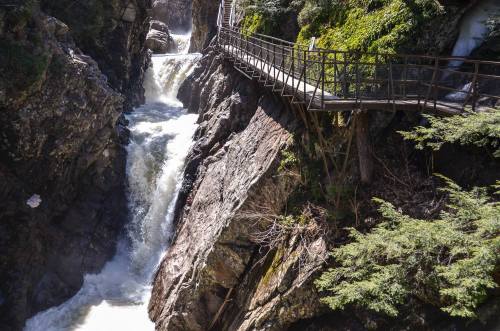 A scenic view of a waterfall cascading between rocky cliffs, with a wooden walkway alongside.