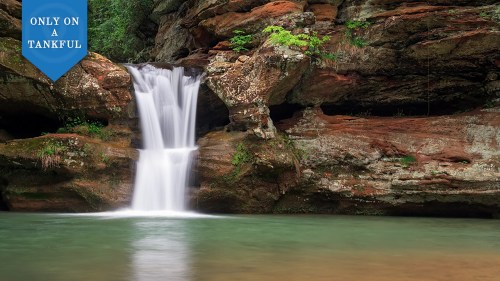 A serene waterfall cascading over rocks into a calm pool, surrounded by lush greenery.