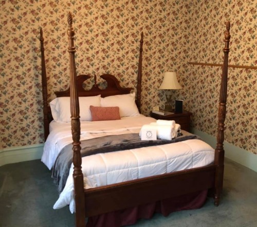 Cozy bedroom featuring a four-poster bed, floral wallpaper, and soft lighting.