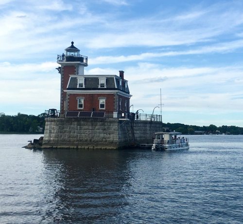 A historic brick lighthouse on a small island, surrounded by water, with a boat approaching nearby.