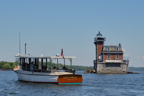A boat named Solaris approaches a historic lighthouse on a sunny day, with clear blue skies and calm waters.