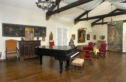A spacious room featuring a grand piano, vintage furniture, and ornate wall decorations in a warm, inviting atmosphere.