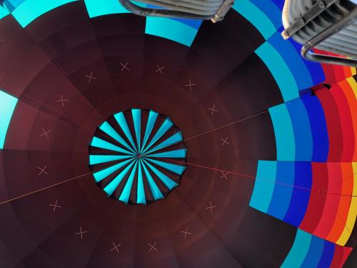 View from inside a hot air balloon, showcasing a vibrant, circular pattern of blue, teal, and red colors.