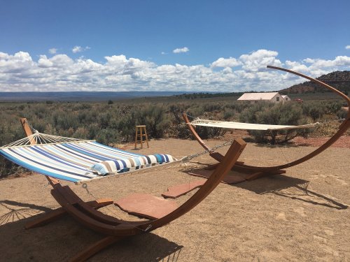 Two hammocks on wooden stands in a desert landscape, with a blue sky and fluffy clouds in the background.