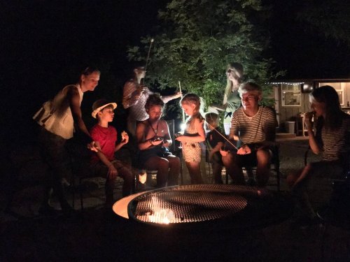 A group of people gathered around a fire pit at night, roasting marshmallows and enjoying each other's company.