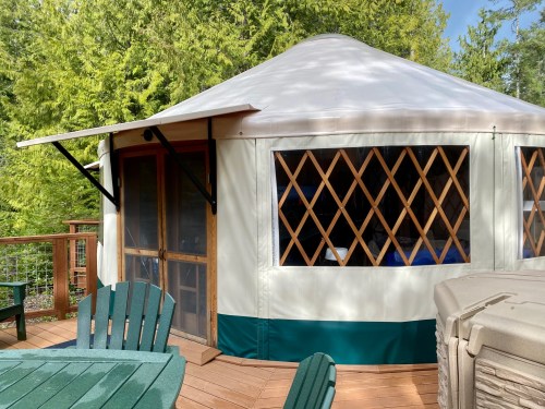 A yurt with a wooden deck surrounded by trees, featuring large windows and a circular roof.
