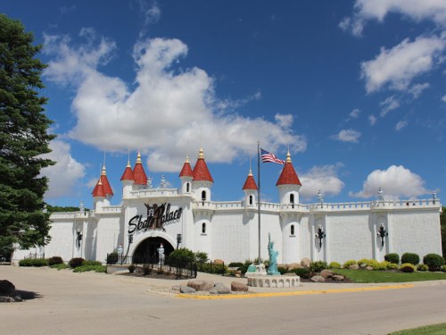 A whimsical castle-like building with red turrets and an American flag, set against a blue sky with fluffy clouds.