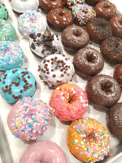 A variety of colorful donuts with sprinkles, chocolate, and cream toppings arranged on a tray.