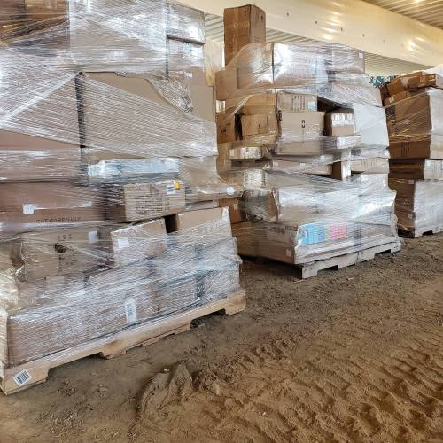 Stacks of cardboard boxes wrapped in plastic, resting on wooden pallets in a warehouse setting.