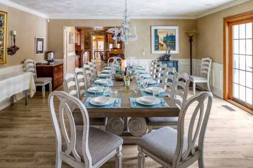 A spacious dining room with a long table set for a meal, featuring elegant chairs and a chandelier above.