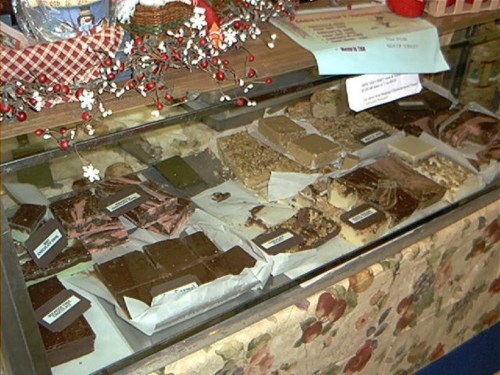 A display case filled with various types of fudge and confections, decorated with festive garlands.