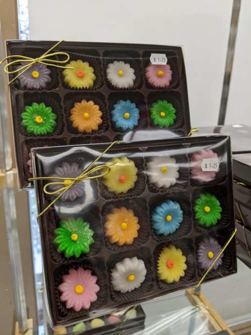 A box of colorful flower-shaped candies arranged in a grid, tied with a gold ribbon.