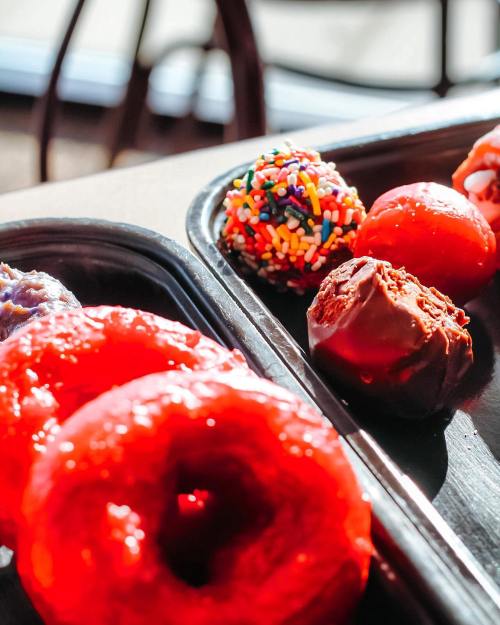 A close-up of colorful donuts and chocolate-covered treats on a black tray, with sprinkles and vibrant red icing.