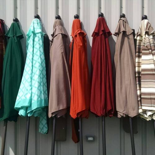 A row of closed patio umbrellas in various colors hanging against a gray wall.