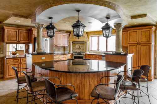 A spacious kitchen with wooden cabinets, a large island, and pendant lights, featuring a warm, inviting design.