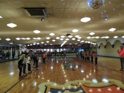 A roller skating rink with children lined up on one side, disco lights reflecting from the ceiling.