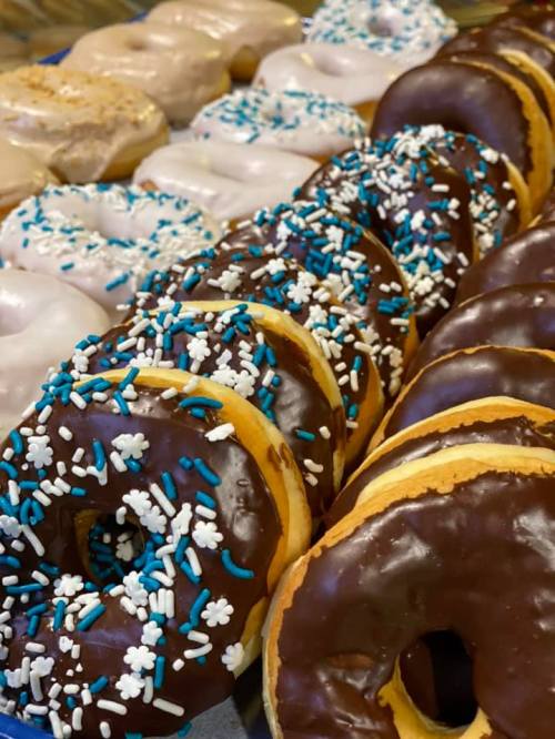 A close-up of assorted donuts, including chocolate-covered and glazed, decorated with blue and white sprinkles.