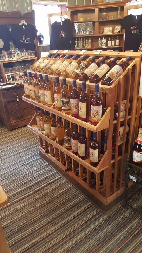 A wooden wine rack displaying various bottles of wine in a cozy shop setting.