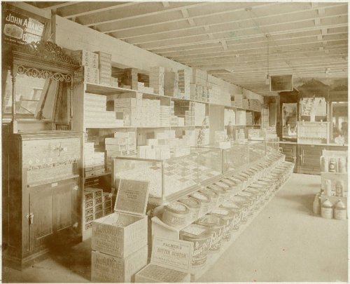 A vintage store interior filled with shelves of boxes and jars, showcasing various goods and a display case.
