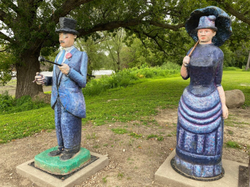 Two colorful, oversized statues of a man in a suit and a woman in a dress, standing on a grassy area.