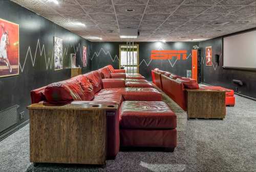 A cozy home theater with red leather couches, dark walls, and ESPN branding, featuring sports-themed decor.