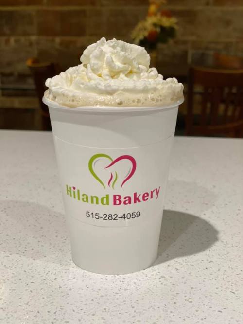 A cup of whipped cream topped beverage from Hiland Bakery, featuring their logo and contact number.