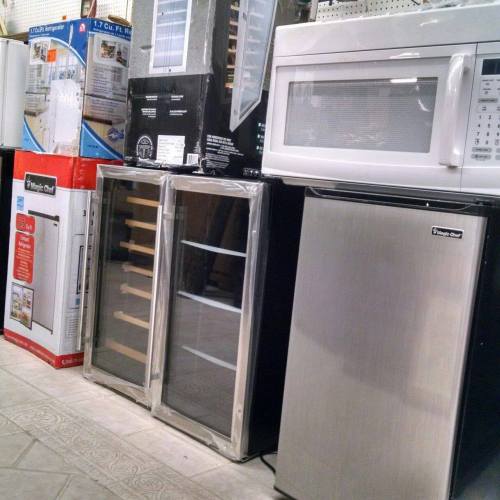 A row of various kitchen appliances, including refrigerators, a wine cooler, and a microwave, displayed in a store.