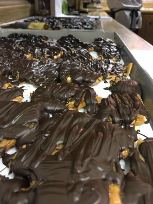 A close-up of trays filled with chocolate-covered treats, showcasing a glossy, dark chocolate coating over crispy bases.