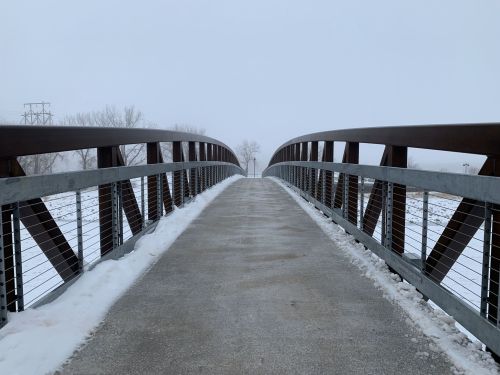 A snow-covered bridge leads into a foggy landscape, with trees barely visible in the distance.
