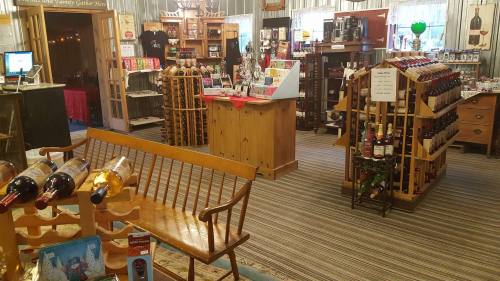 A cozy shop interior featuring wine displays, shelves of gifts, and a wooden bench in a warm, inviting atmosphere.