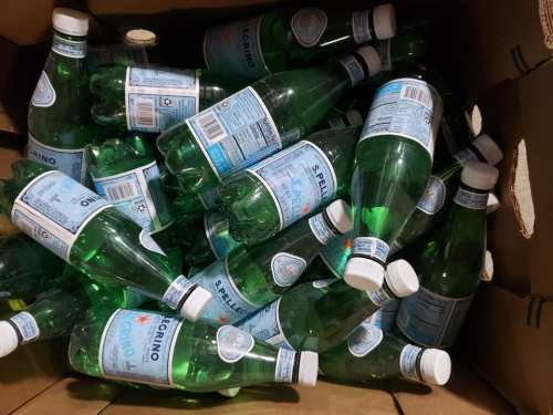 A box filled with green glass bottles of sparkling water, some labels visible, arranged haphazardly.