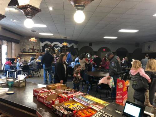 A busy community hall with people socializing, tables set up, and snacks displayed in the foreground.
