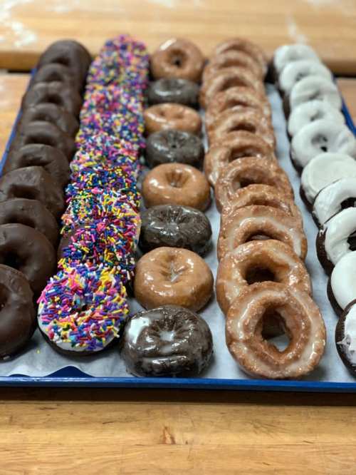 A tray of assorted donuts, including chocolate, glazed, and sprinkled varieties, arranged in neat rows.