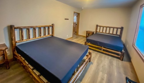 A simple room featuring two wooden-framed beds with dark mattresses and a window, creating a cozy atmosphere.