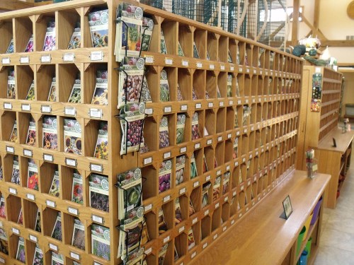 A wooden display filled with packets of seeds organized in cubbyholes, showcasing various flower and vegetable varieties.