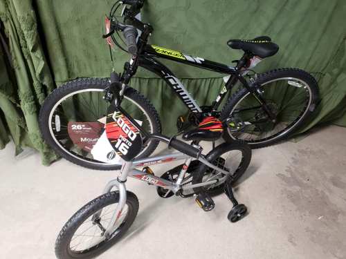 Two bicycles: a black mountain bike with yellow accents and a smaller silver bike with training wheels, both on a concrete floor.