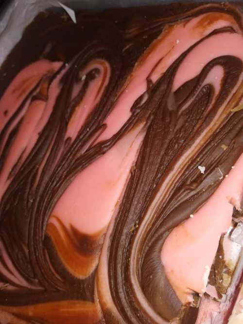 A close-up of a dessert with swirls of chocolate and pink frosting, creating a marbled effect.