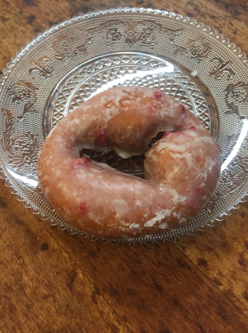 A glazed donut with pink sprinkles on a decorative glass plate, resting on a wooden table.