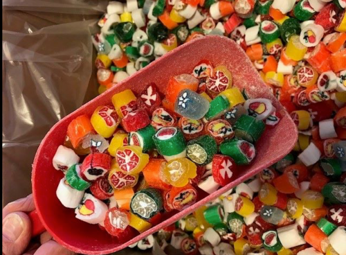 A red scoop filled with colorful, assorted candies, surrounded by more candies in the background.
