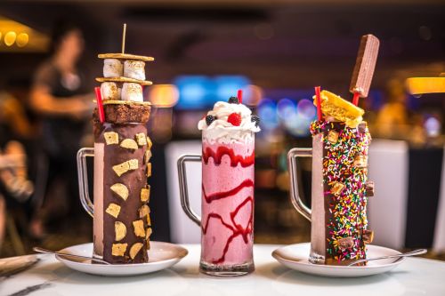 Three colorful milkshakes topped with various treats, including whipped cream, sprinkles, and cookies, on a table.