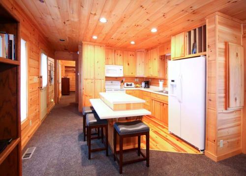 Cozy wooden kitchen with a central island, bar stools, and modern appliances in a rustic cabin setting.