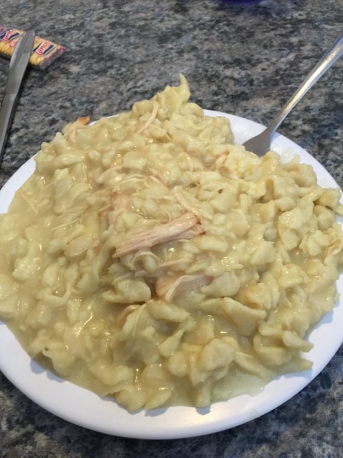 A plate of creamy chicken and dumplings on a granite countertop, with a fork beside it.