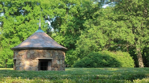 A small stone structure with a conical roof surrounded by lush greenery and trees.
